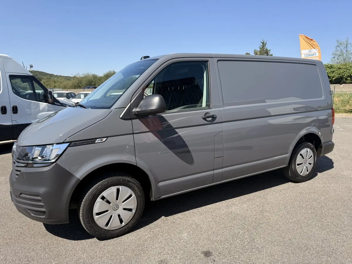 Vue de profil côté gauche d’un Volkswagen Transporter gris clair 2023, fourgon utilitaire avec jantes acier et vitres avant teintées.