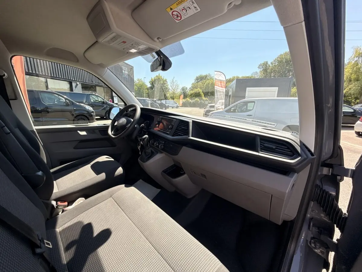 Vue intérieure côté conducteur du Volkswagen Transporter gris clair 2023, mettant en valeur le tableau de bord et les sièges avant.
