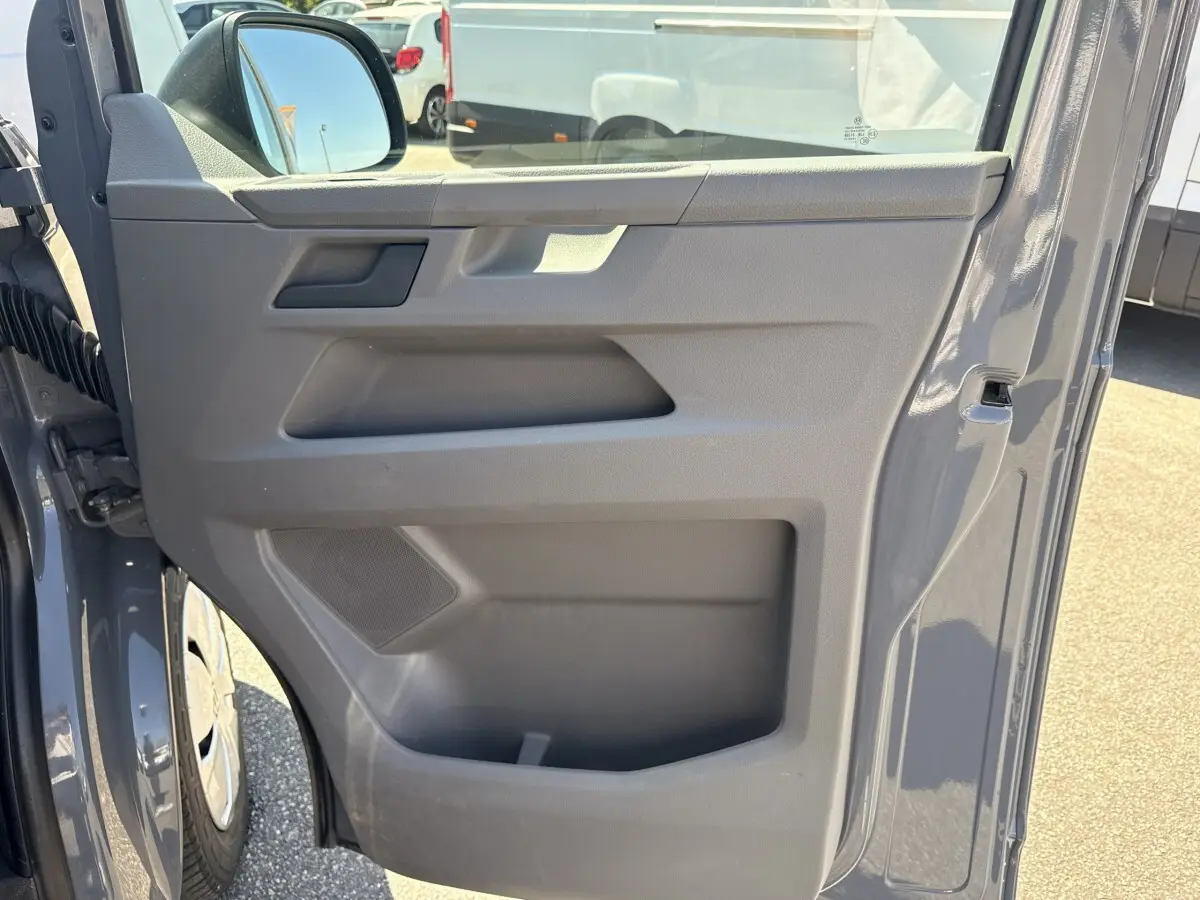 Vue rapprochée de la porte avant gauche gris clair du Volkswagen Transporter 2023 avec rétroviseur électrique et rangement intégré.