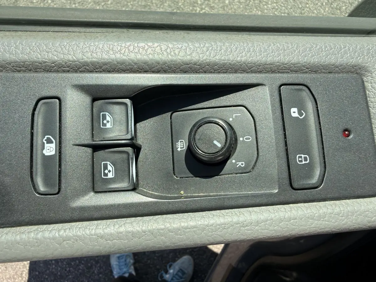 Gros plan sur les commandes de réglage des rétroviseurs et des vitres côté conducteur du Volkswagen Transporter gris clair 2023.