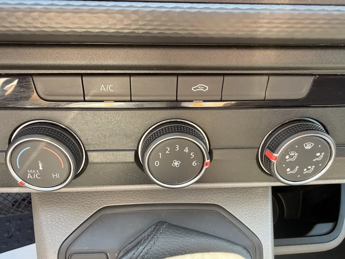 Gros plan sur les commandes de climatisation du Volkswagen Transporter gris clair, avec boutons rotatifs et touches A/C et recyclage d'air.