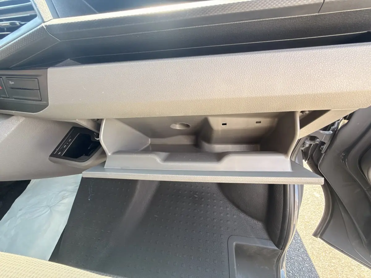 Vue intérieure côté passager du Volkswagen Transporter gris clair 2023, boîte auto, avec boîte à gants ouverte et plancher visible.