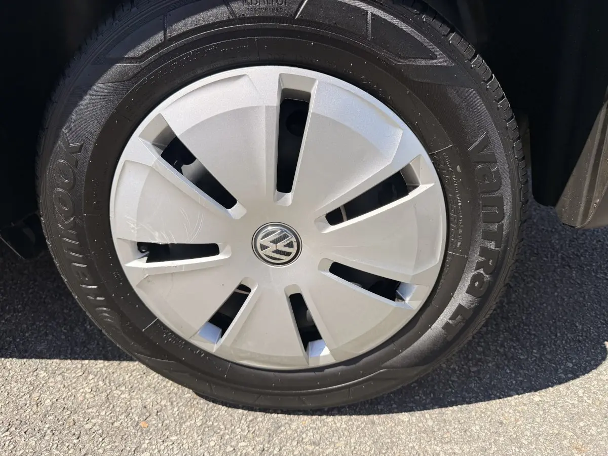 Gros plan sur la roue avant droite du Volkswagen Transporter gris clair, avec enjoliveur argenté et logo VW central.