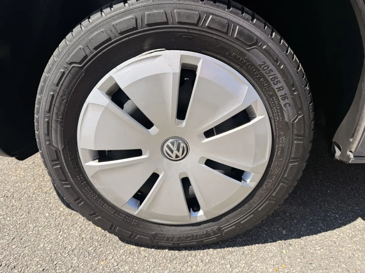 Gros plan sur la roue avant droite du Volkswagen Transporter gris clair, avec enjoliveur argenté et logo VW central.