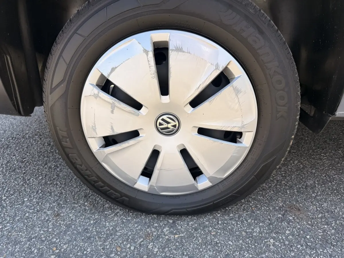 Gros plan sur la roue avant droite du Volkswagen Transporter gris clair, avec enjoliveur marqué du logo VW.