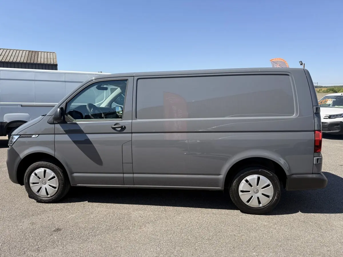 Vue de profil côté gauche d’un Volkswagen Transporter gris clair 2023, fourgon utilitaire avec jantes acier et vitres teintées.