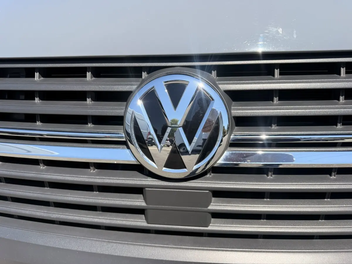 Gros plan sur la calandre grise claire du Volkswagen Transporter 2023 avec logo VW chromé brillant au centre.