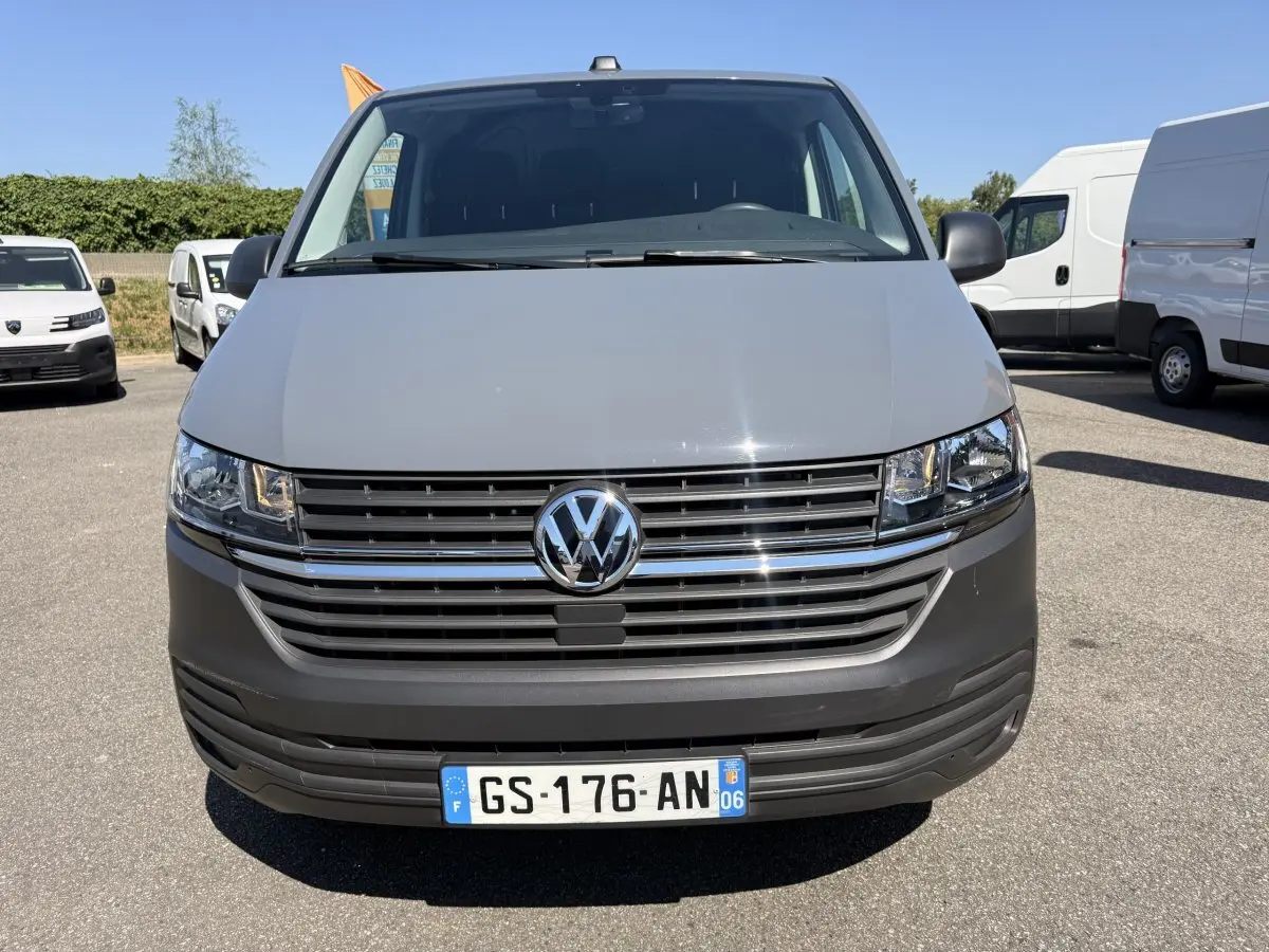 Vue de face d'un Volkswagen Transporter gris clair 2023 avec calandre chromée et plaque d'immatriculation française.
