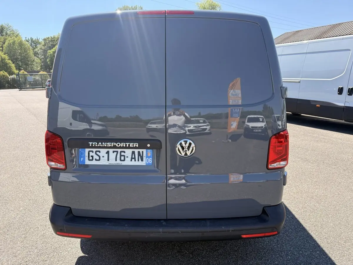 Vue arrière d’un Volkswagen Transporter gris clair 2023 avec portes battantes et feux rouges visibles.