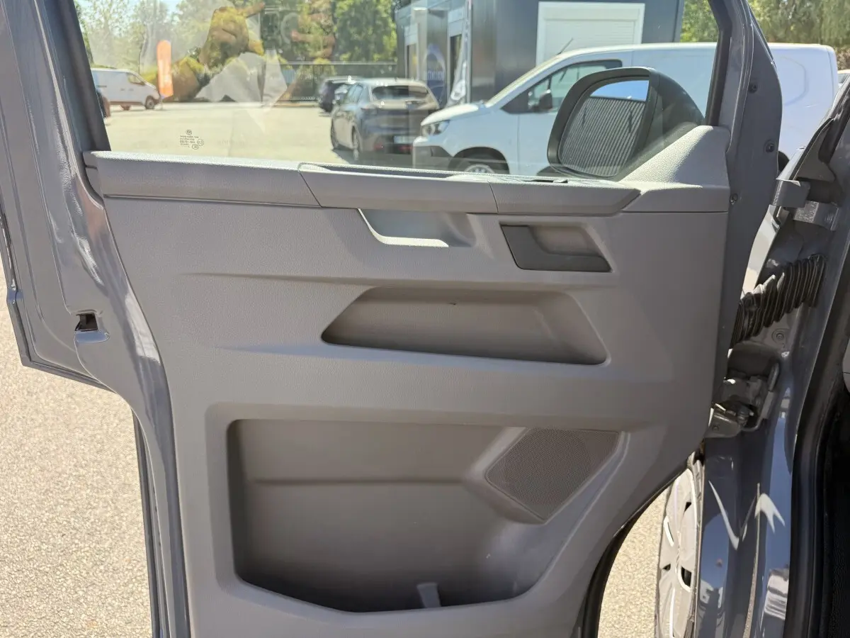 Vue rapprochée de la porte avant droite gris clair du Volkswagen Transporter 2023, avec poignée et haut-parleur intégrés.