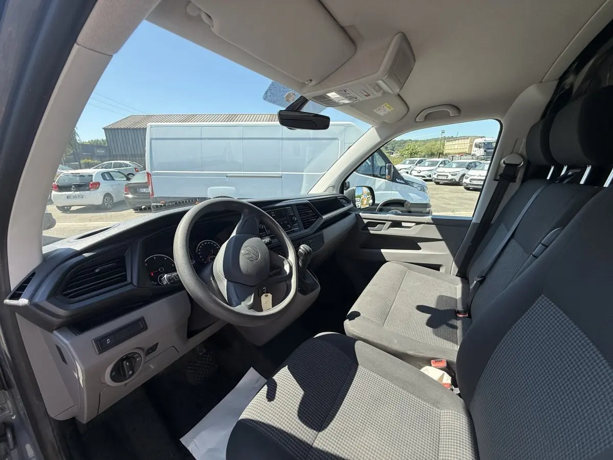 Vue intérieure côté conducteur du Volkswagen Transporter gris clair 2023, montrant le tableau de bord et les sièges avant.