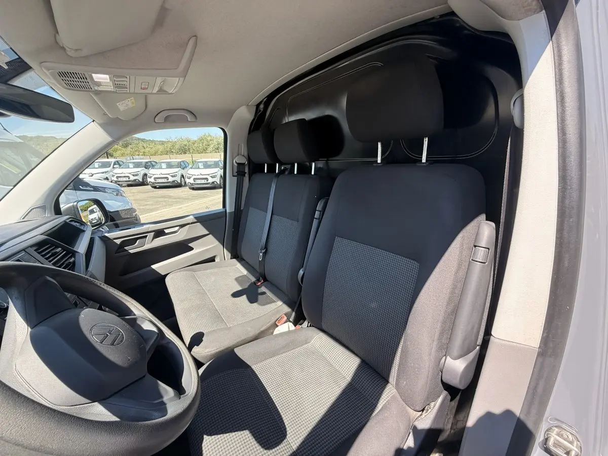 Vue intérieure côté conducteur du Volkswagen Transporter gris clair 2023, montrant les sièges avant et le tableau de bord.