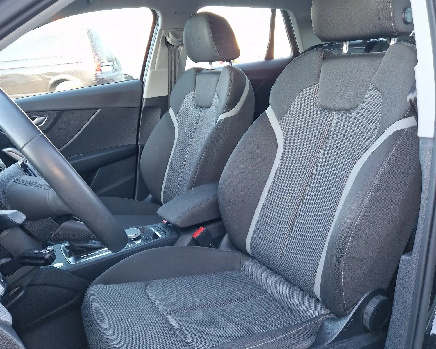 Vue intérieure côté conducteur de l'Audi Q2 35 TFSI 2021 noire, sièges sport en tissu gris avec surpiqûres claires.