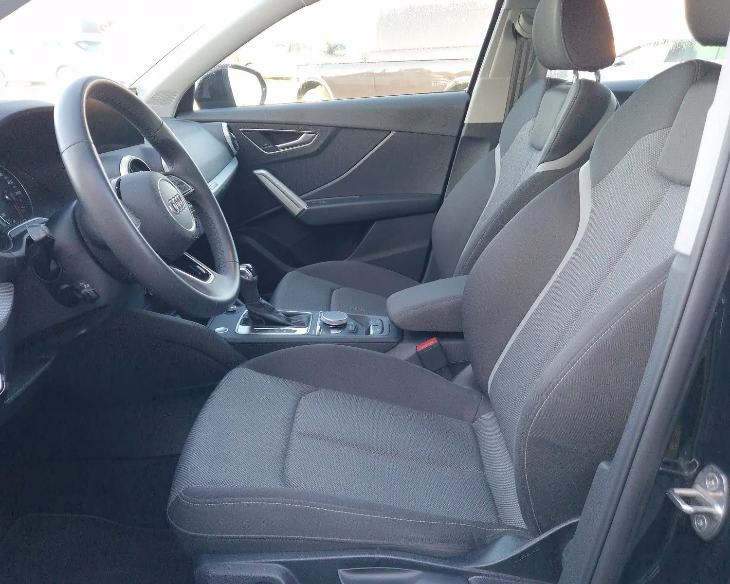 Vue intérieure côté conducteur de l'Audi Q2 noire, montrant sièges en tissu et tableau de bord moderne.