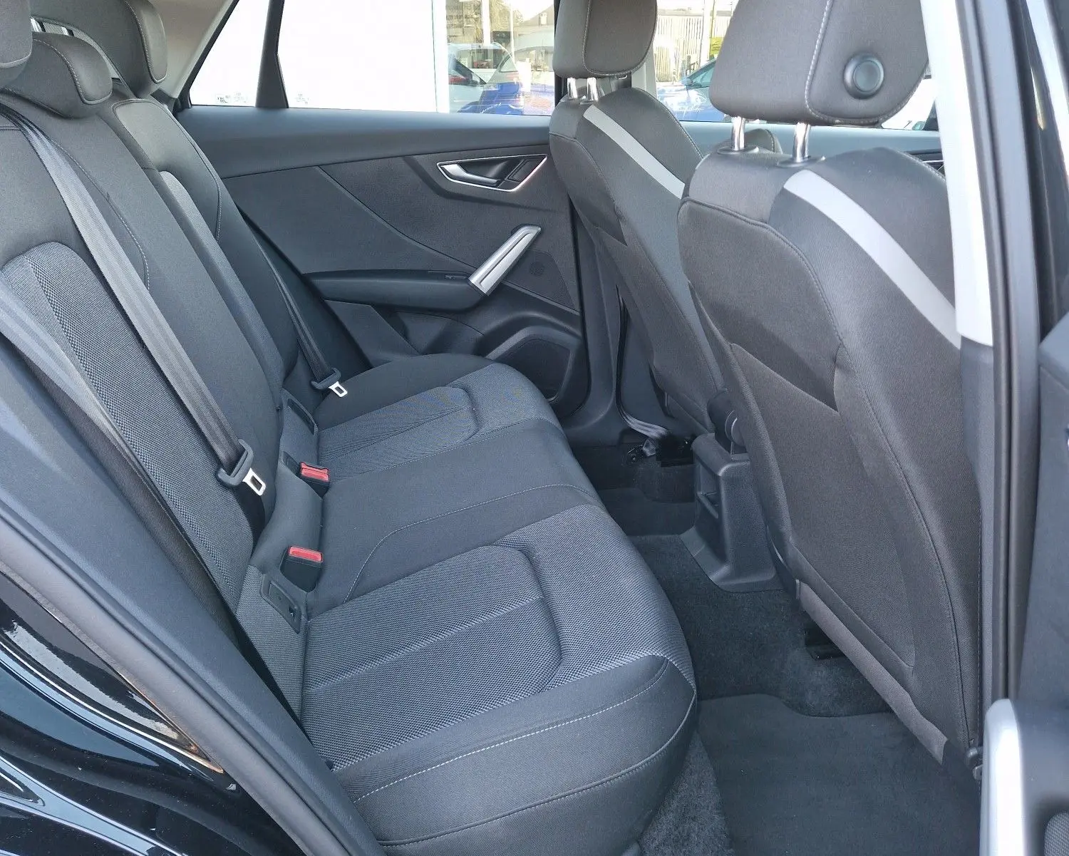 Vue intérieure arrière côté gauche de l'Audi Q2 noire, montrant les sièges arrière en tissu et les appuie-têtes réglables.
