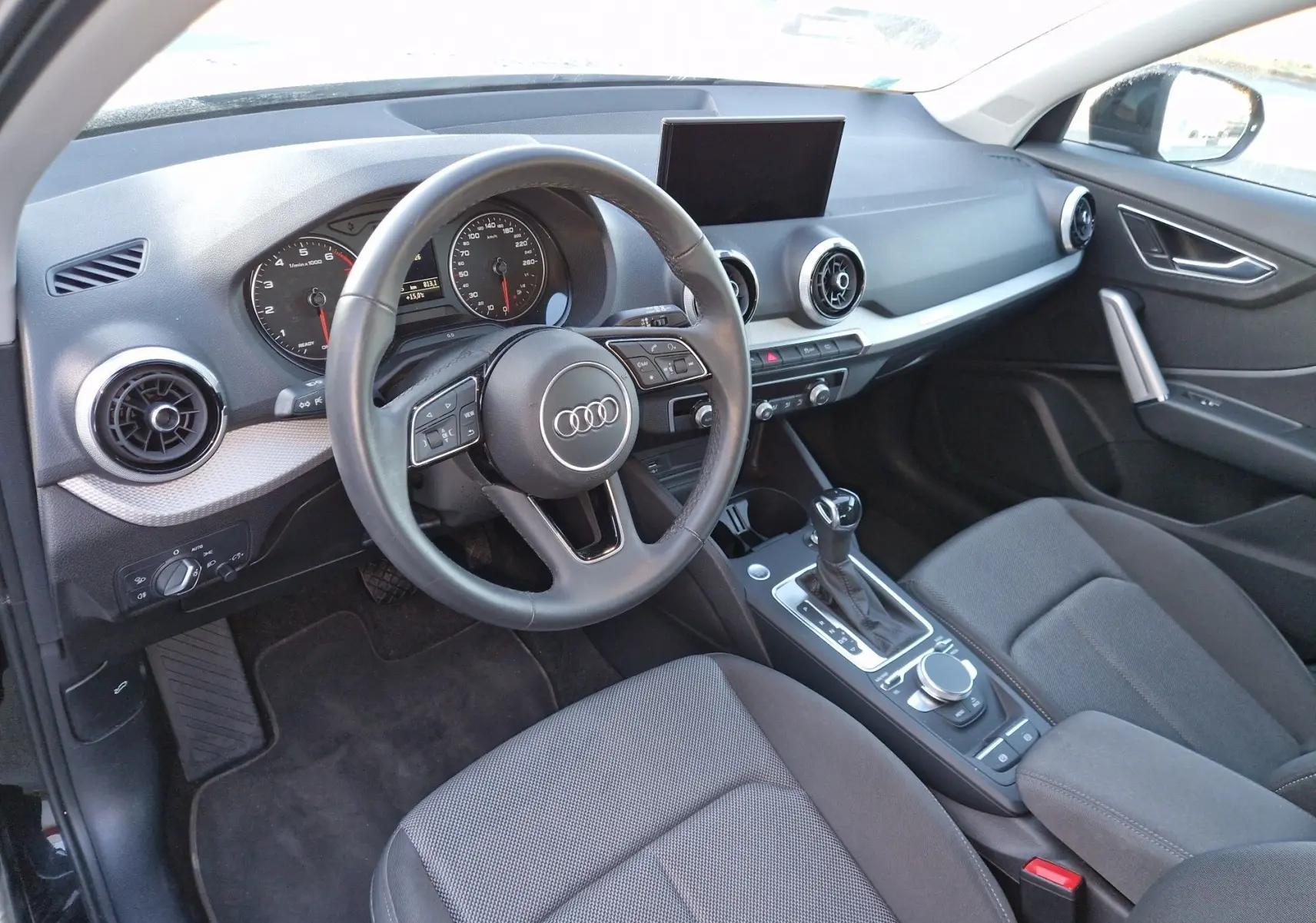 Vue intérieure de l'Audi Q2 35 TFSI 2021, côté conducteur, avec tableau de bord noir et écran central déployé.