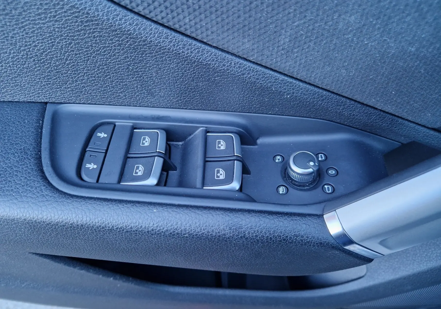 Gros plan sur les commandes de lève-vitres et réglage des rétroviseurs côté gauche d’un Audi Q2 noir.