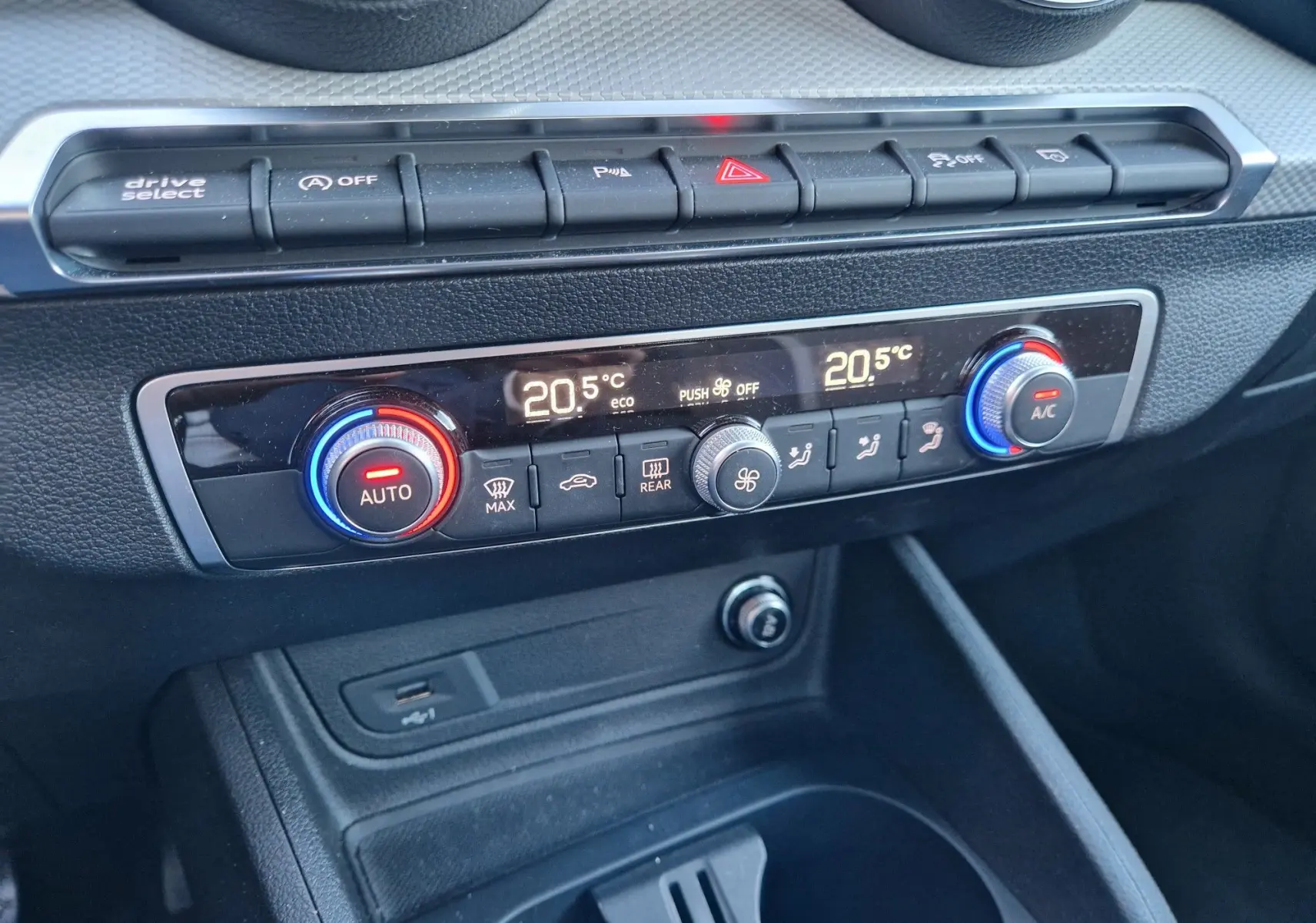 Gros plan sur la console centrale de l'Audi Q2 noire, montrant les commandes de climatisation digitale à 20,5°C.