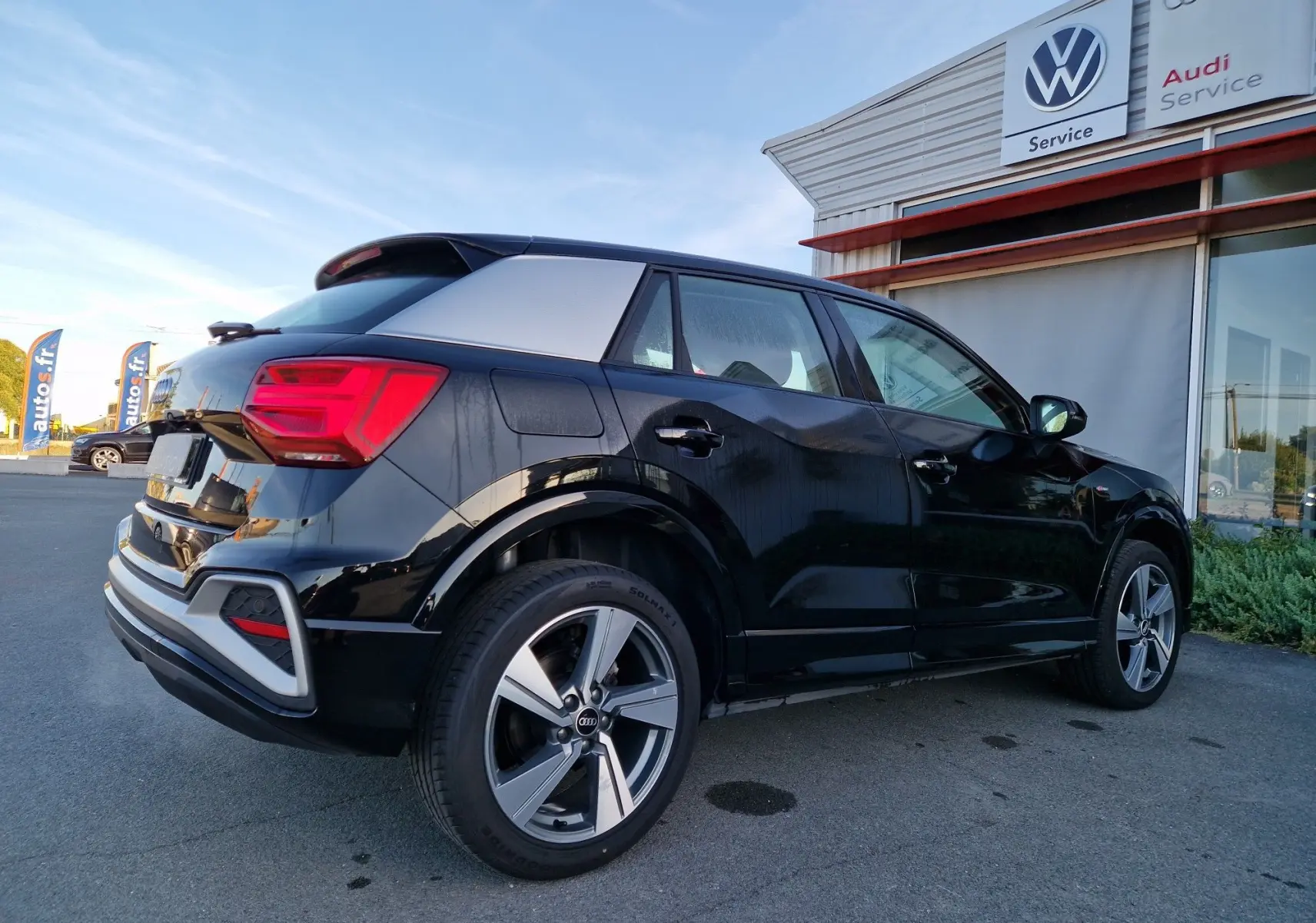 Audi Q2 35 TFSI noir vue 3/4 arrière droit, toit contrasté argent, jantes alliage et feux LED visibles.