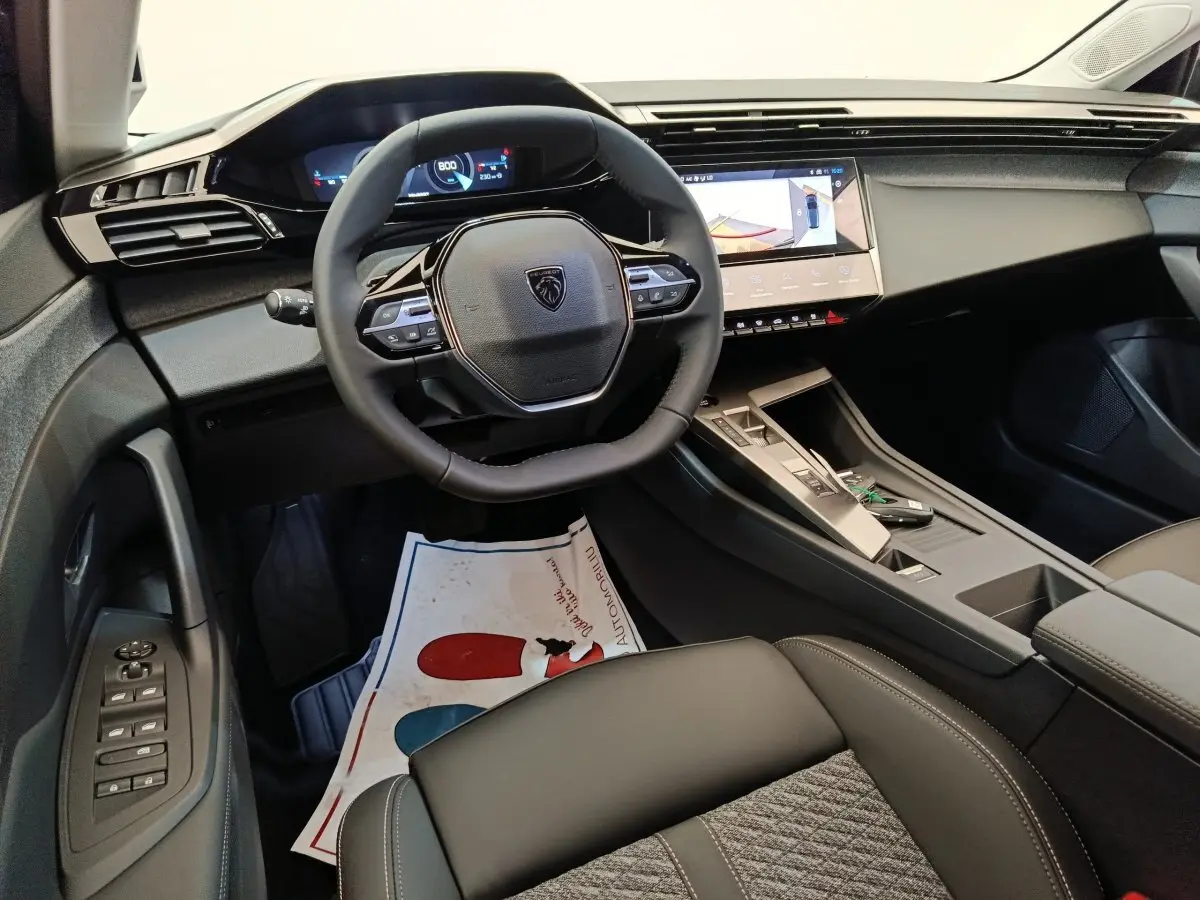 Vue intérieure côté conducteur du Peugeot 308 2026 gris foncé, volant cuir multifonctions et écran tactile central visible.