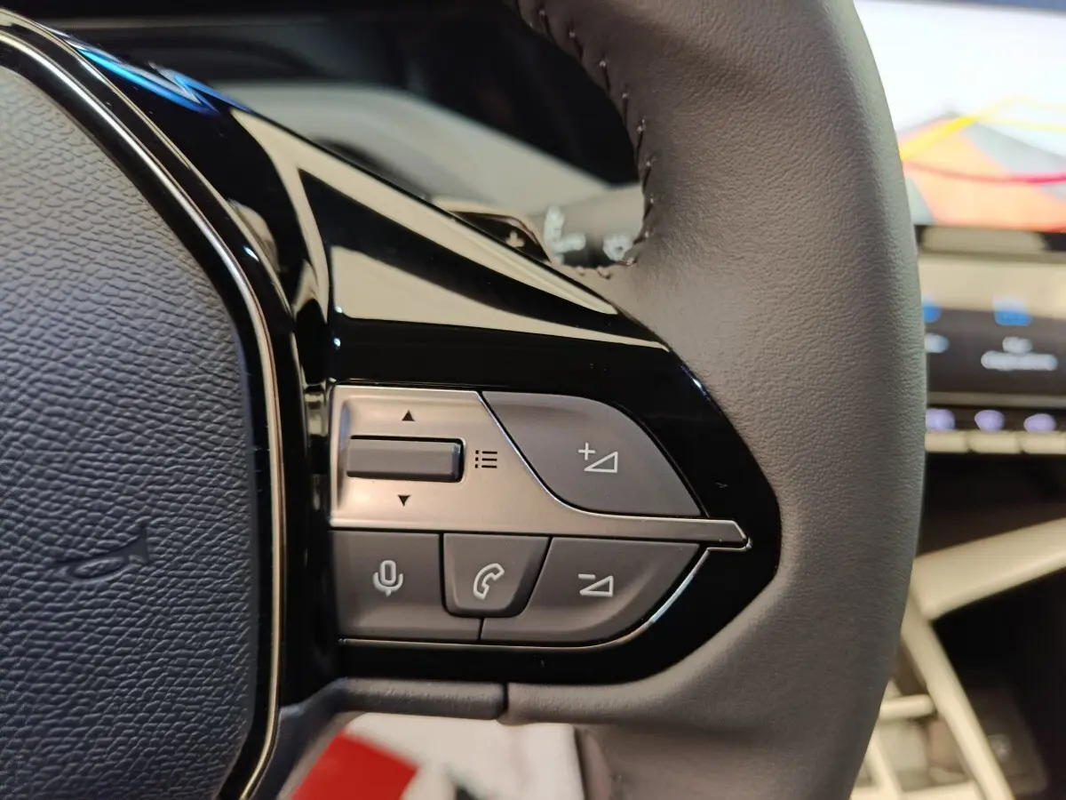 Gros plan sur le volant cuir gris foncé de la Peugeot 308 2026, avec commandes multifonctions visibles.
