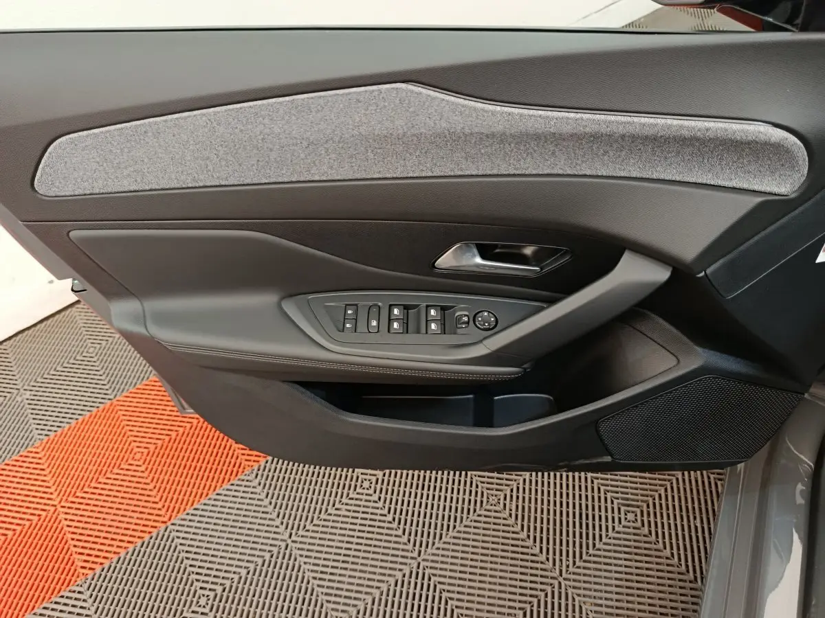 Vue intérieure côté gauche de la porte avant d'une Peugeot 308 gris foncé avec commandes de vitres et poignée métallique.