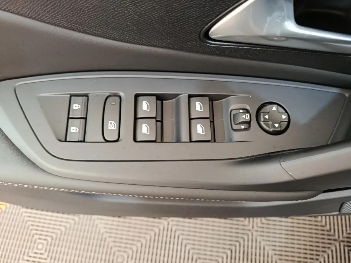 Gros plan sur les commandes de lève-vitres et réglages des rétroviseurs côté conducteur d’une Peugeot 308 gris foncé 2026.