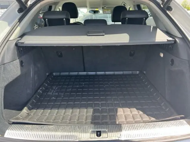 Coffre ouvert d'un Audi Q3 blanc 2015, vue arrière montrant l'espace de chargement avec tapis de protection noir.
