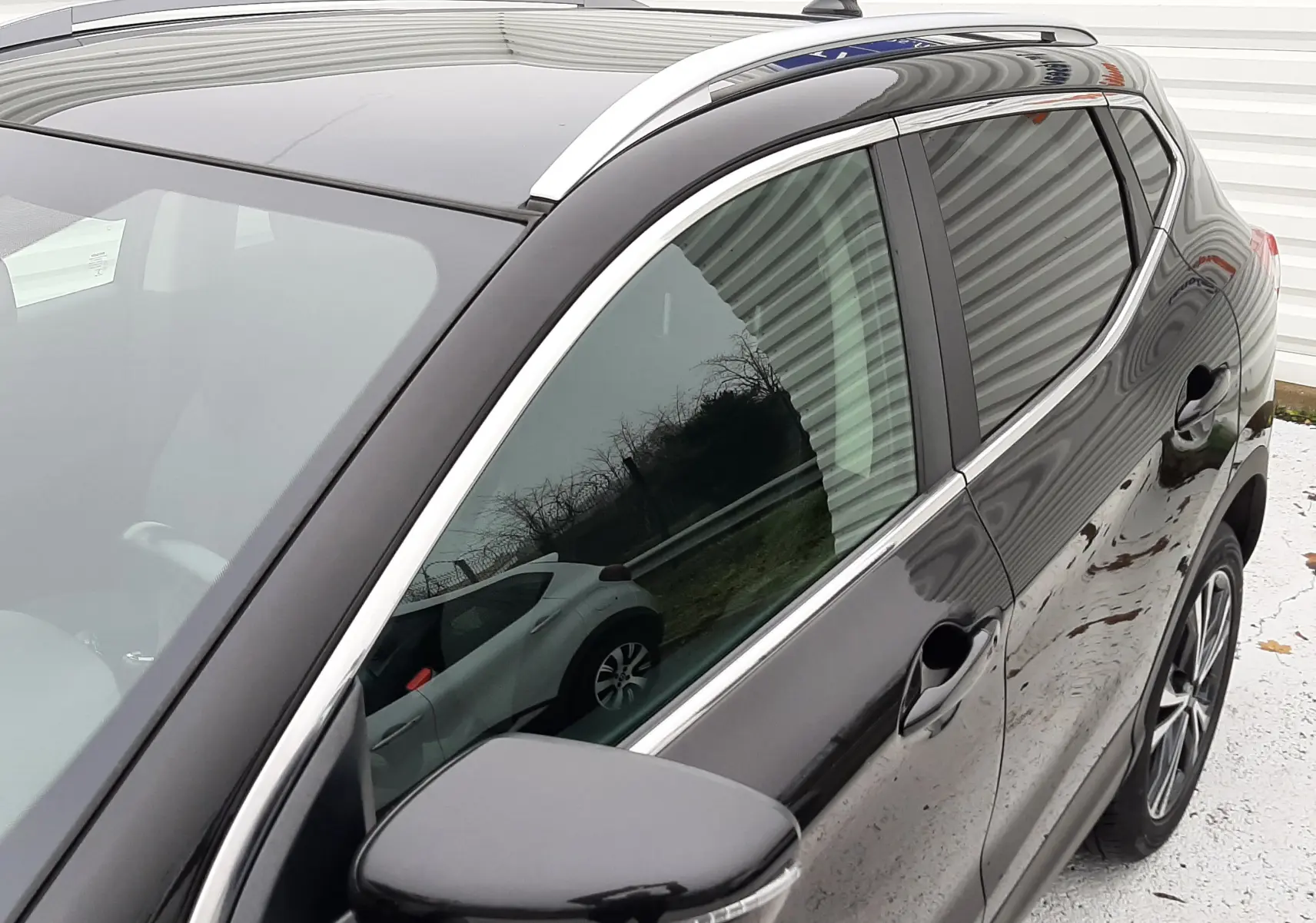 Vue de profil avant droit du Nissan Qashqai noir 2020, mettant en valeur la finition brillante et les barres de toit argentées.