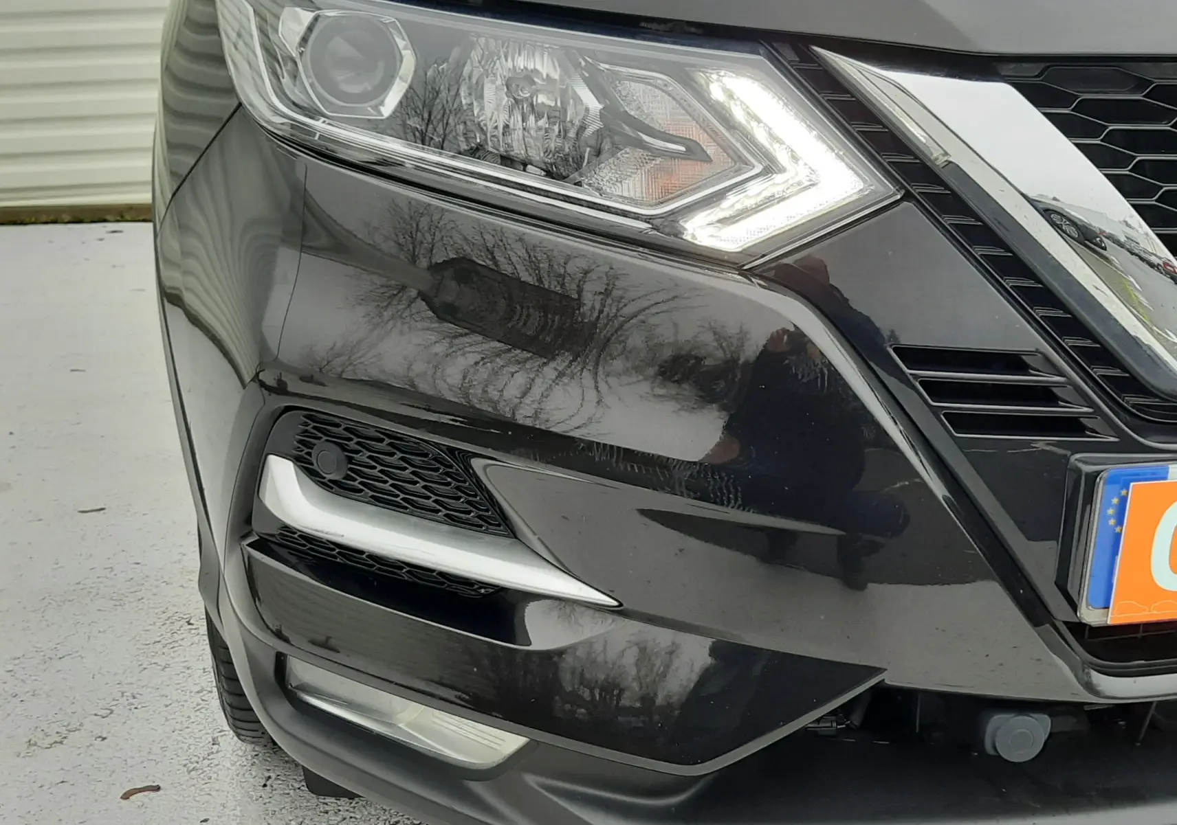 Gros plan sur l'avant droit noir d'un Nissan Qashqai 2020, mettant en valeur le phare LED allumé et la calandre chromée.