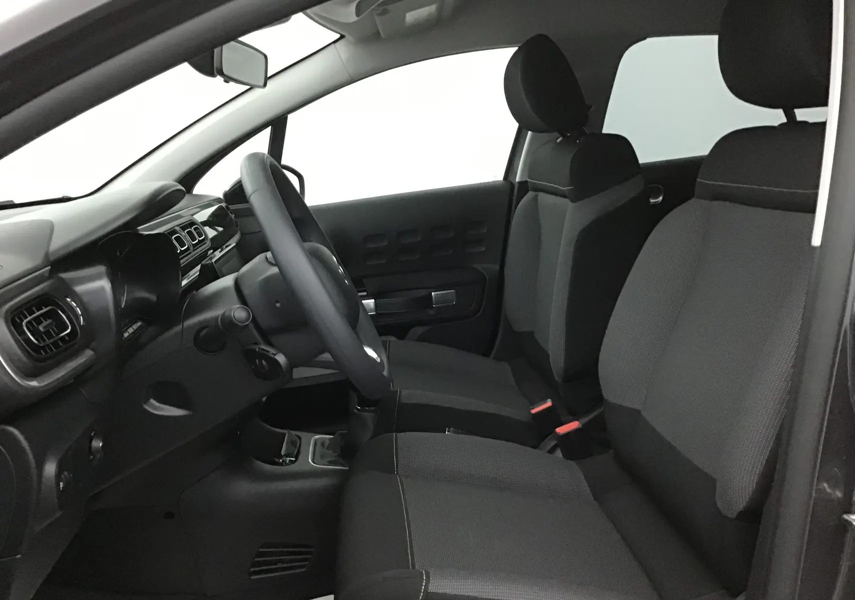 Intérieur de la Citroën C3 2022 vu côté conducteur, sièges tissu gris et tableau de bord noir épuré.