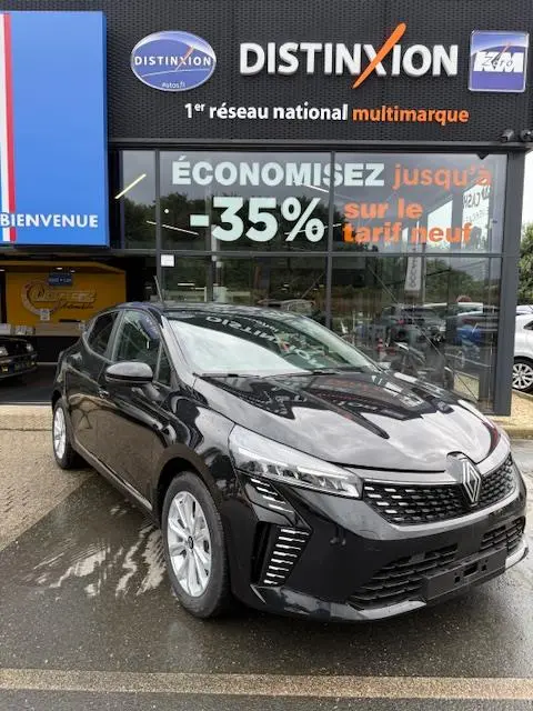 Renault Clio Evolution Blue dCi 100 noire vue 3/4 avant, calandre chromée et feux LED distinctifs, devant un showroom multimarque.