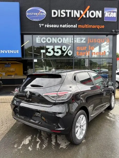 Vue 3/4 arrière droite d'une Renault Clio noire Evolution Blue dCi 100, stationnée devant un concessionnaire multimarque.