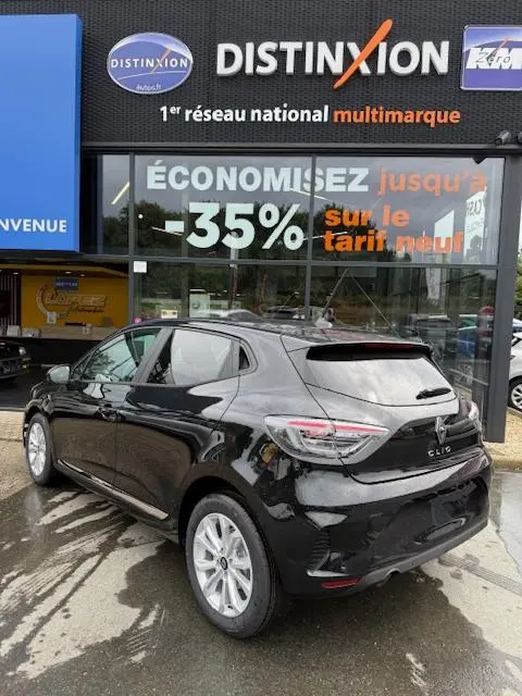 Renault Clio noire vue en 3/4 arrière droit, avec feux LED et jantes alliage, devant une vitrine commerciale.