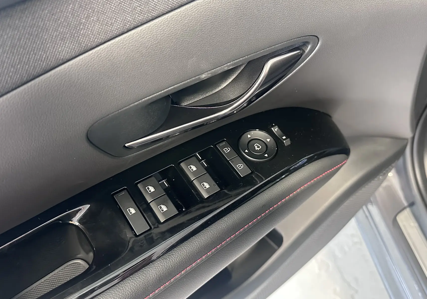 Gros plan sur la porte côté conducteur du Hyundai Tucson gris Ecotronic, montrant les commandes des vitres et le bouton de réglage des rétroviseurs.