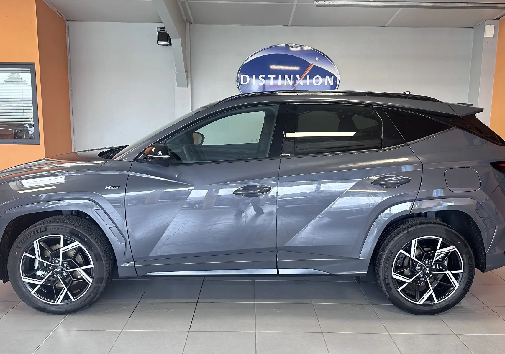 Vue de profil côté gauche du Hyundai Tucson 1.6 T-GDI gris Ecotronic avec jantes alliage noires et toit noir.