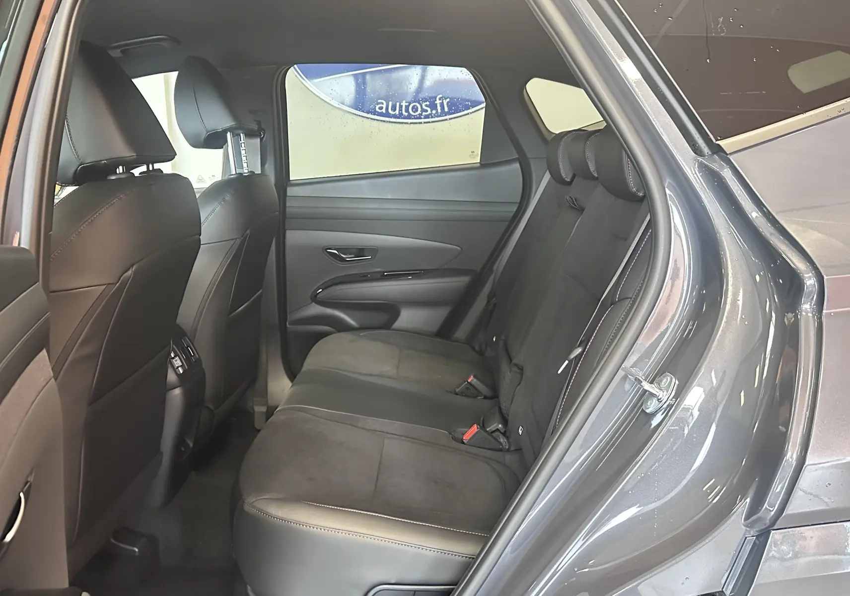 Vue intérieure côté droit des sièges arrière en cuir noir du Hyundai Tucson 2025 gris Ecotronic, porte arrière ouverte.