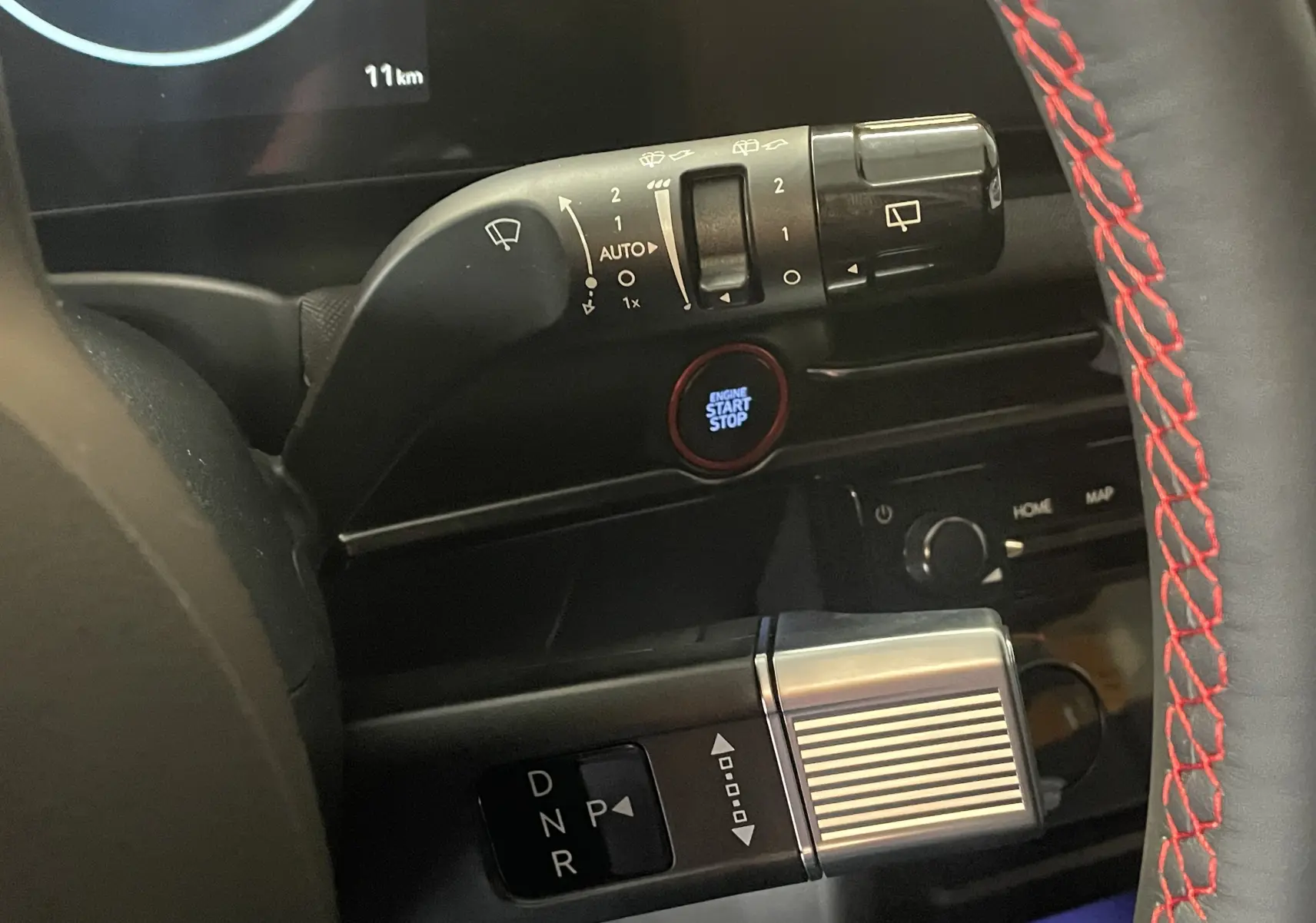 Gros plan sur la commande de boîte automatique et le bouton start/stop du Hyundai Tucson 2025, volant avec surpiqûres rouges.