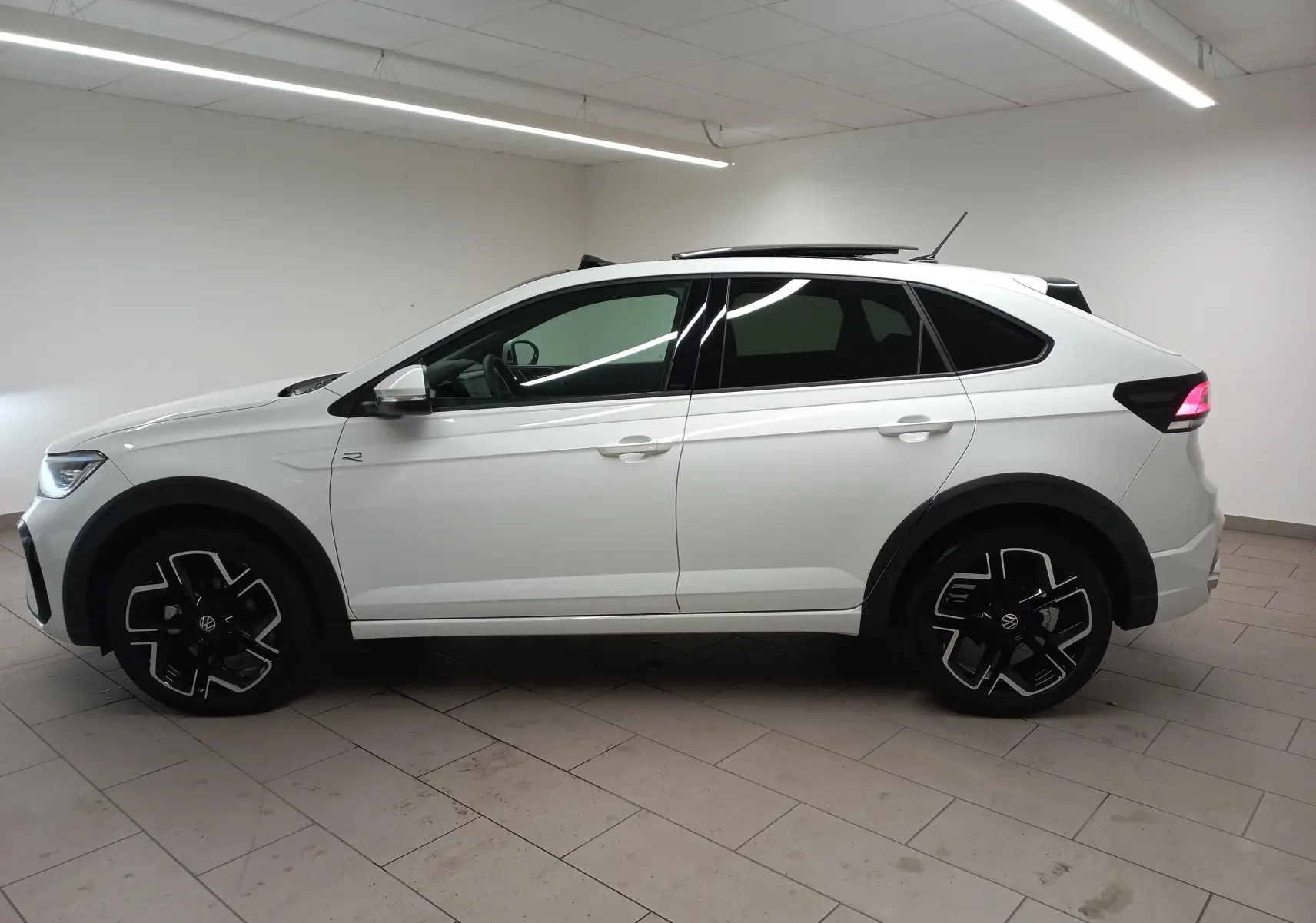 Volkswagen Taigo blanc pur en profil droit, avec jantes noires et toit ouvrant partiellement ouvert.