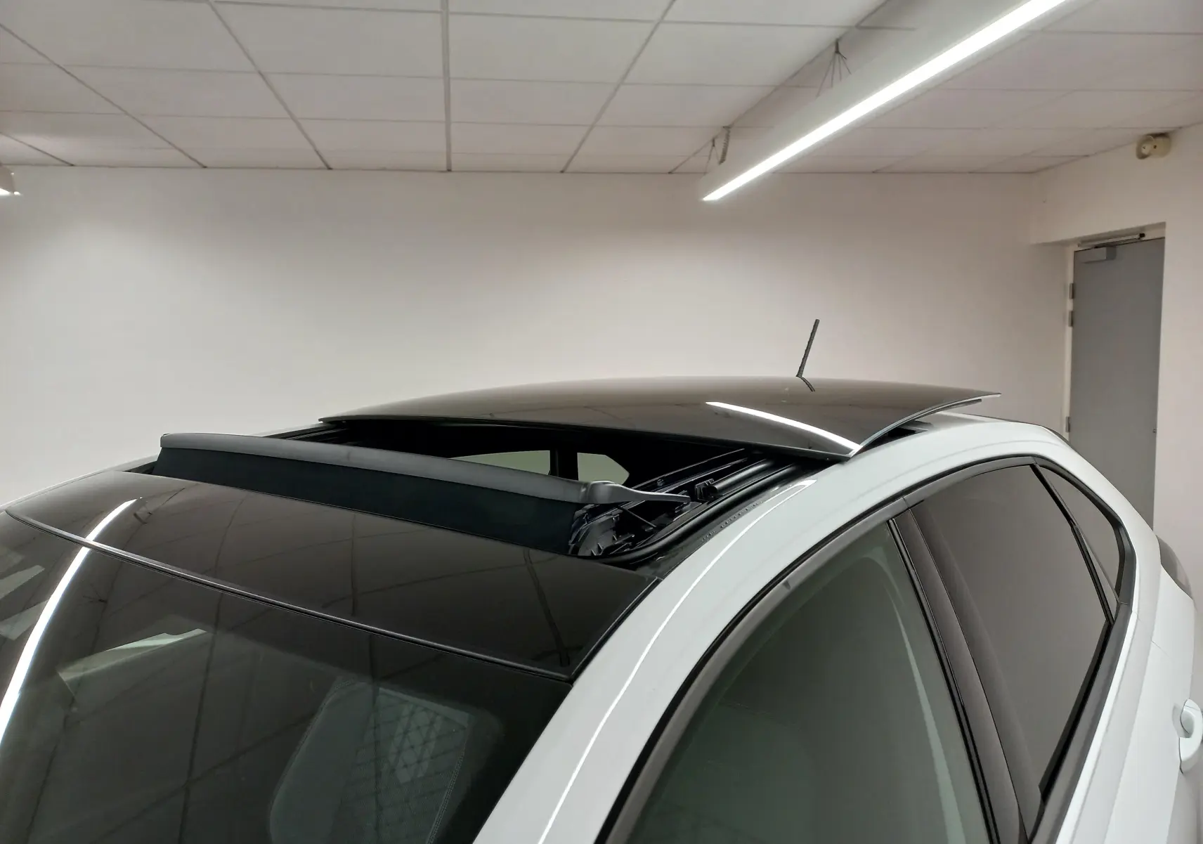 Vue rapprochée du toit ouvrant ouvert sur le côté gauche d’un Volkswagen Taigo blanc pur 2025 en intérieur.