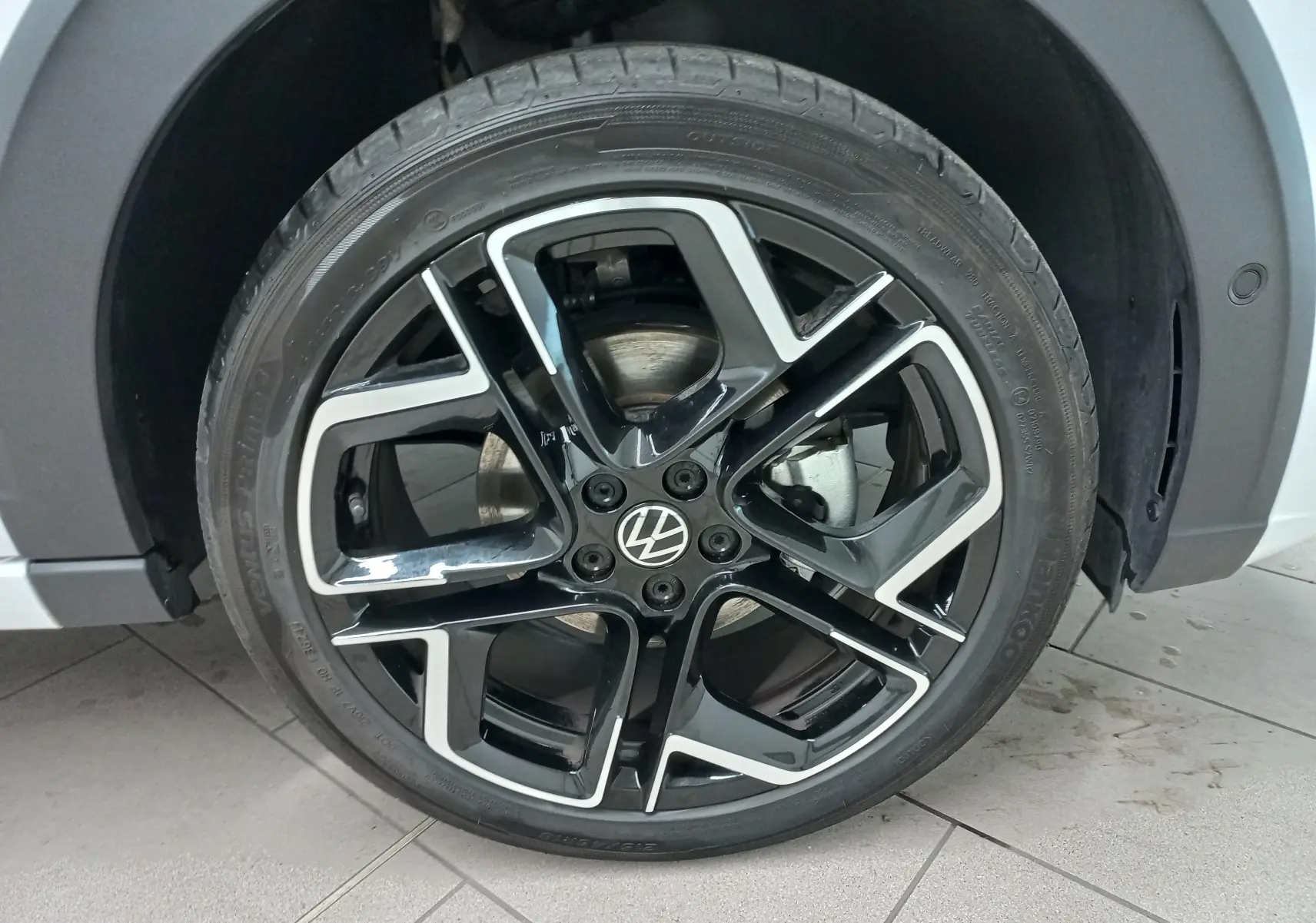 Gros plan sur la roue avant droite du Volkswagen Taigo blanc pur 2025 avec jante alliage noir et argent R-Line.