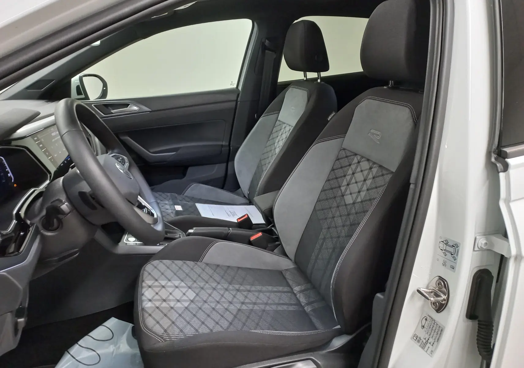 Vue intérieure côté conducteur du Volkswagen Taigo blanc pur 2025, sièges sport R-LINE avec motifs géométriques distinctifs.