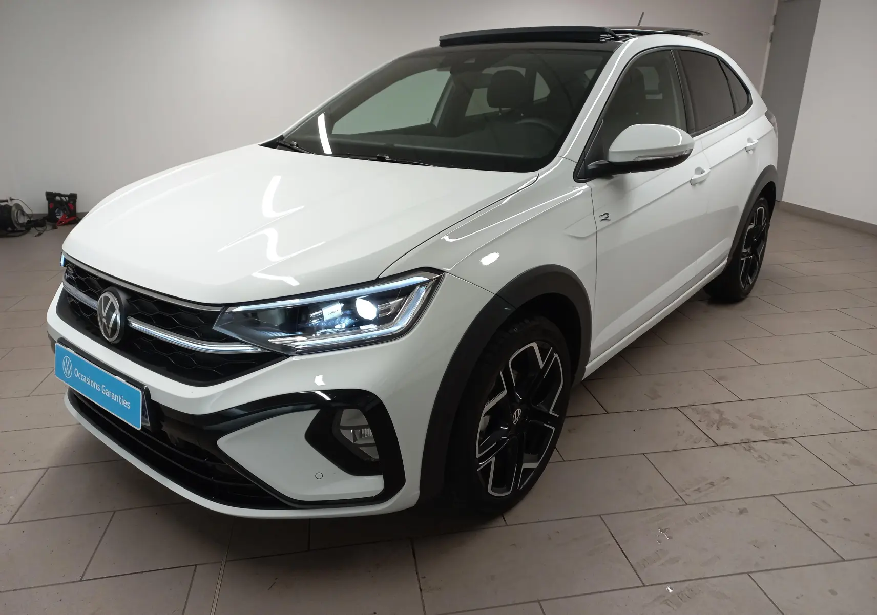 Volkswagen Taigo blanc pur en 3/4 avant droit, version R-Line avec toit ouvrant et jantes noires distinctives.