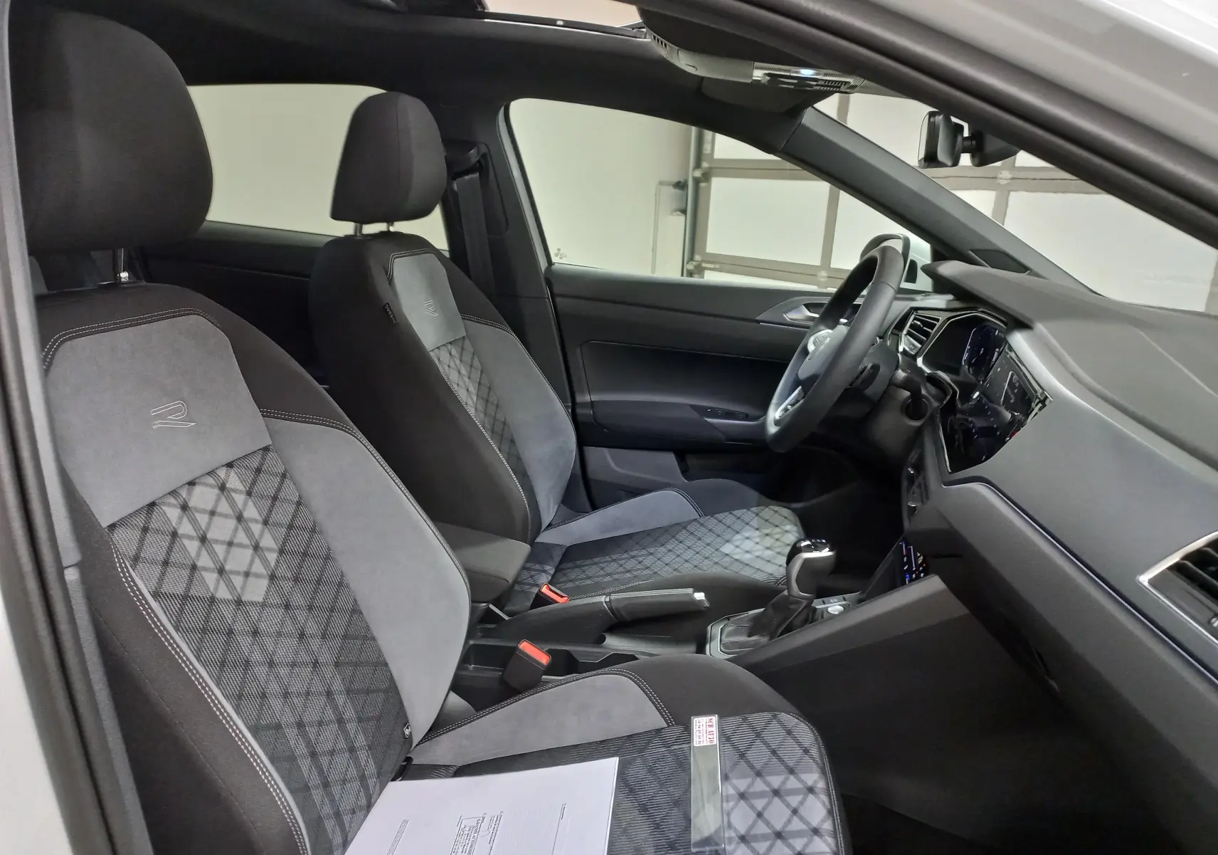 Intérieur côté conducteur du Volkswagen Taigo blanc 2025, sièges R-Line en tissu gris avec toit ouvrant visible.