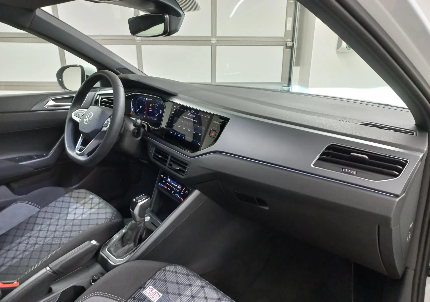 Vue intérieure côté conducteur du Volkswagen Taigo blanc pur 2025, mettant en valeur le tableau de bord digital et la console centrale avec boîte auto.