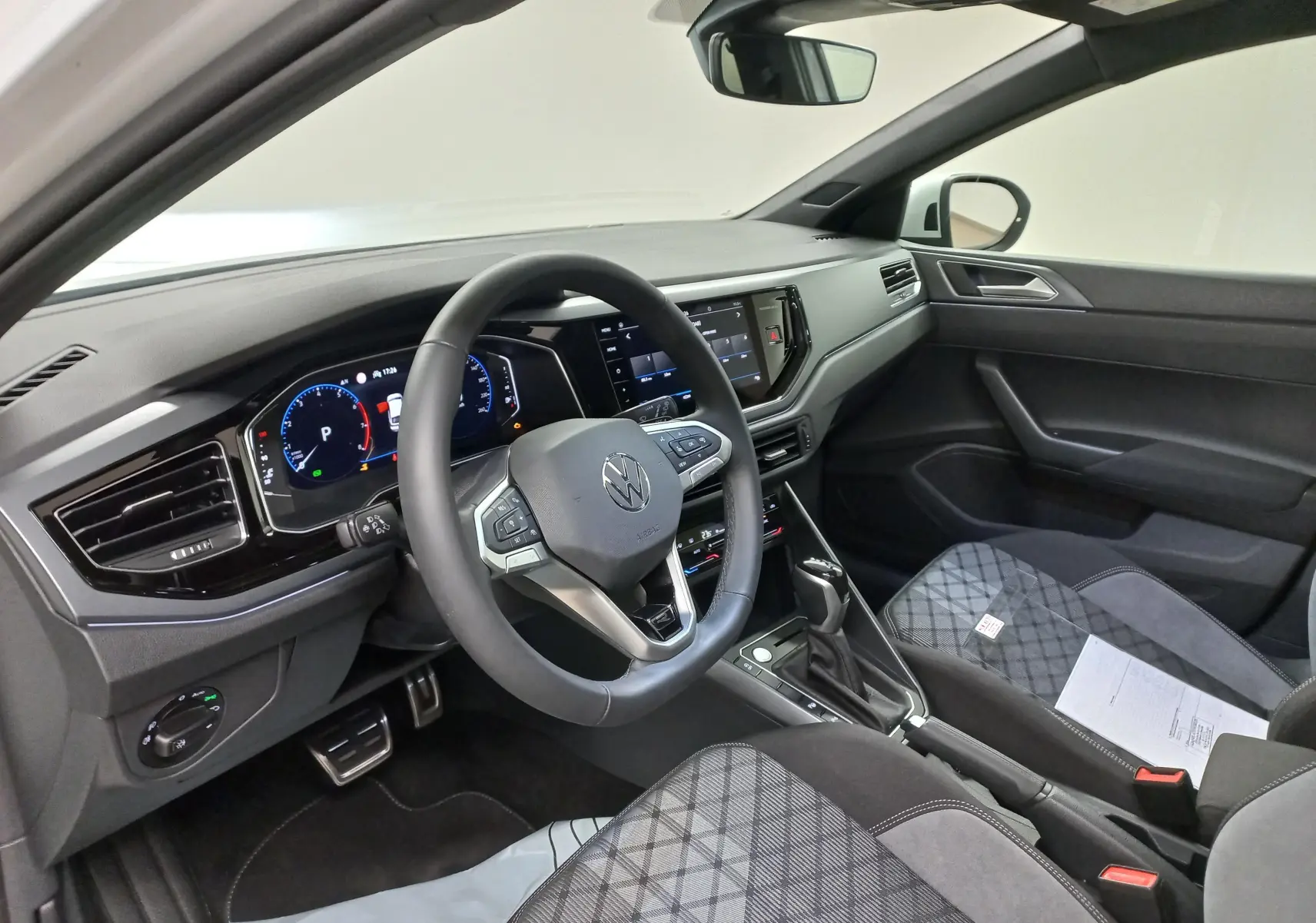 Vue intérieure côté conducteur du Volkswagen Taigo 2025 avec volant multifonction, tableau de bord digital et sièges tissu à motifs.