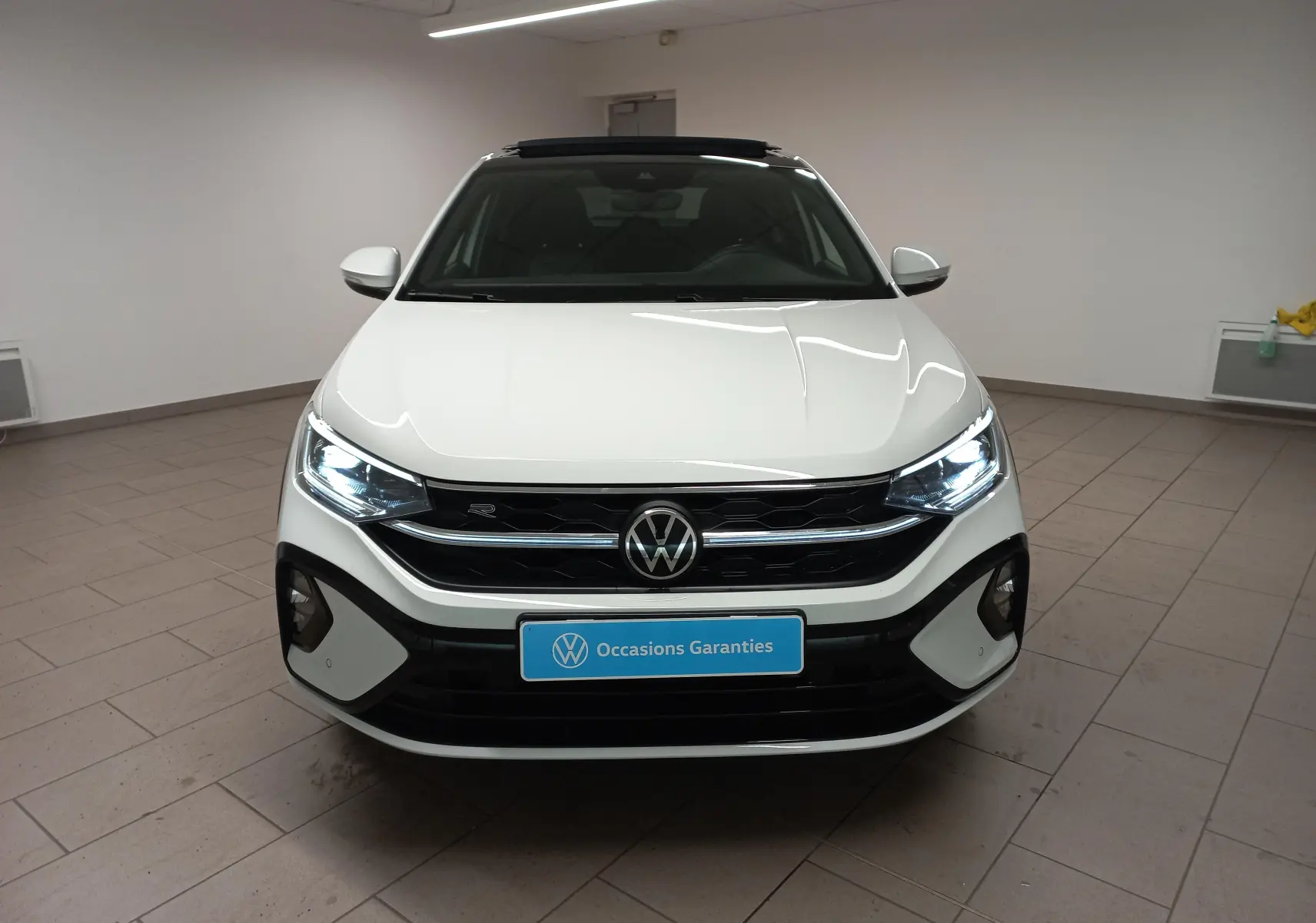 Vue frontale d'un Volkswagen Taigo blanc pur 2025 avec toit ouvrant et finition R-Line, phares allumés en intérieur.