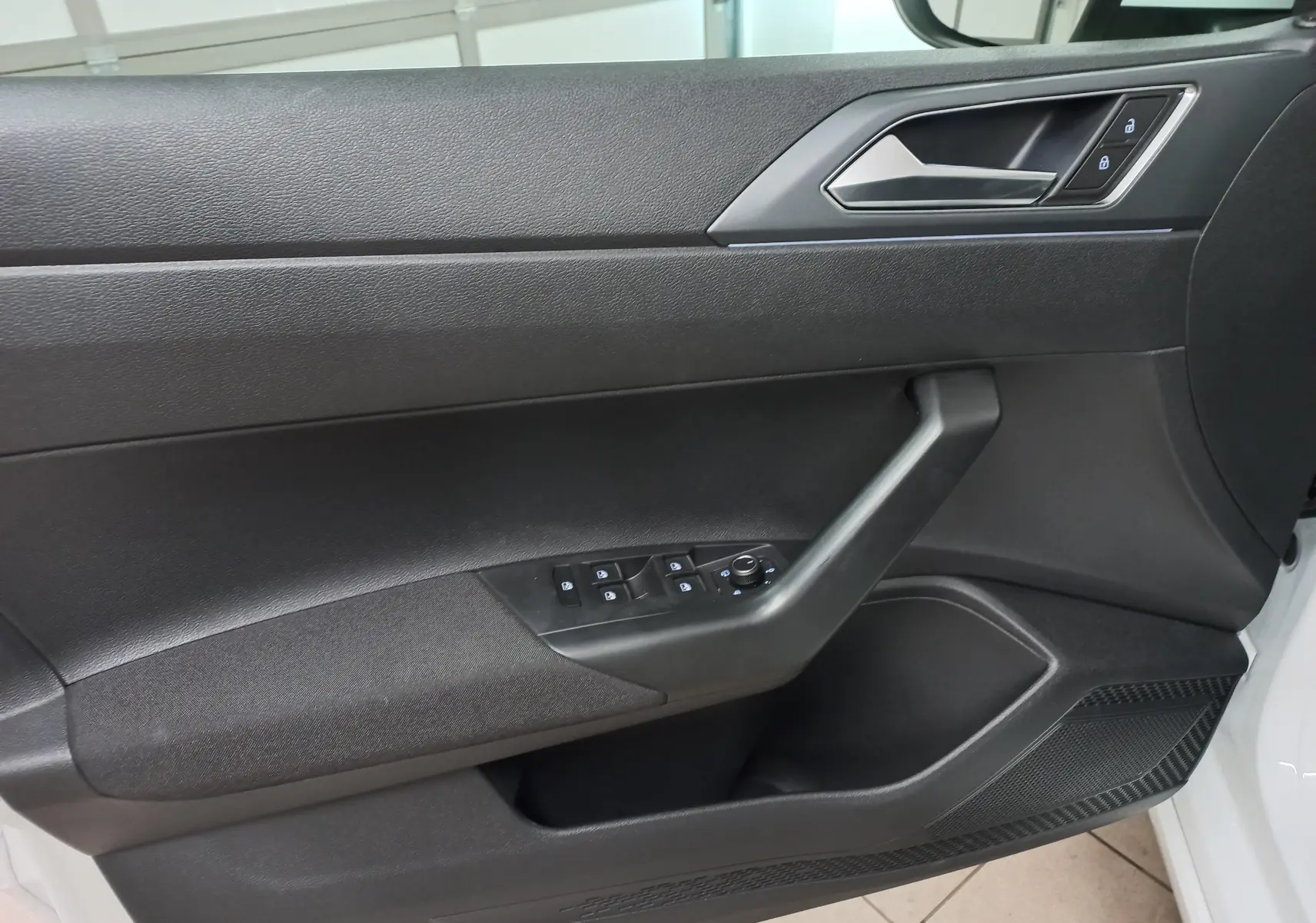 Vue intérieure du panneau de porte côté gauche du Volkswagen Taigo blanc pur 2025, avec commandes électriques et poignée noire.