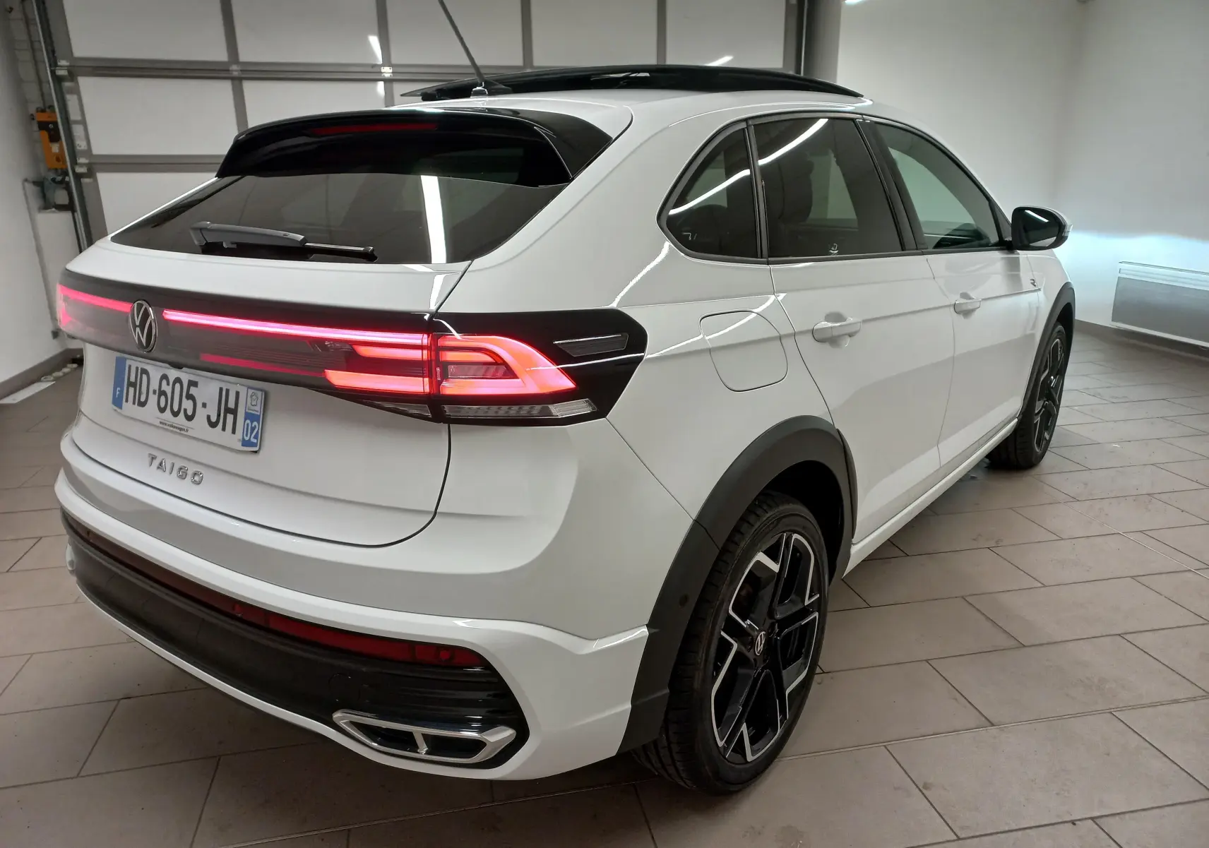 Volkswagen Taigo blanc pur 2025 en vue 3/4 arrière droit, avec feux LED allumés et toit ouvrant noir.