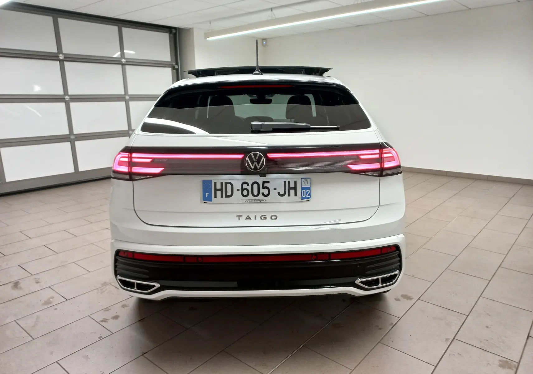 Vue arrière d'un Volkswagen Taigo blanc pur 2025 avec feux LED allumés et double sortie d'échappement chromée.